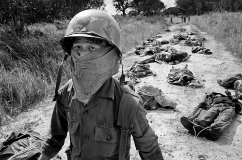 Foto van een vietnamese soldaat met achter zich verschillende dode soldaten.